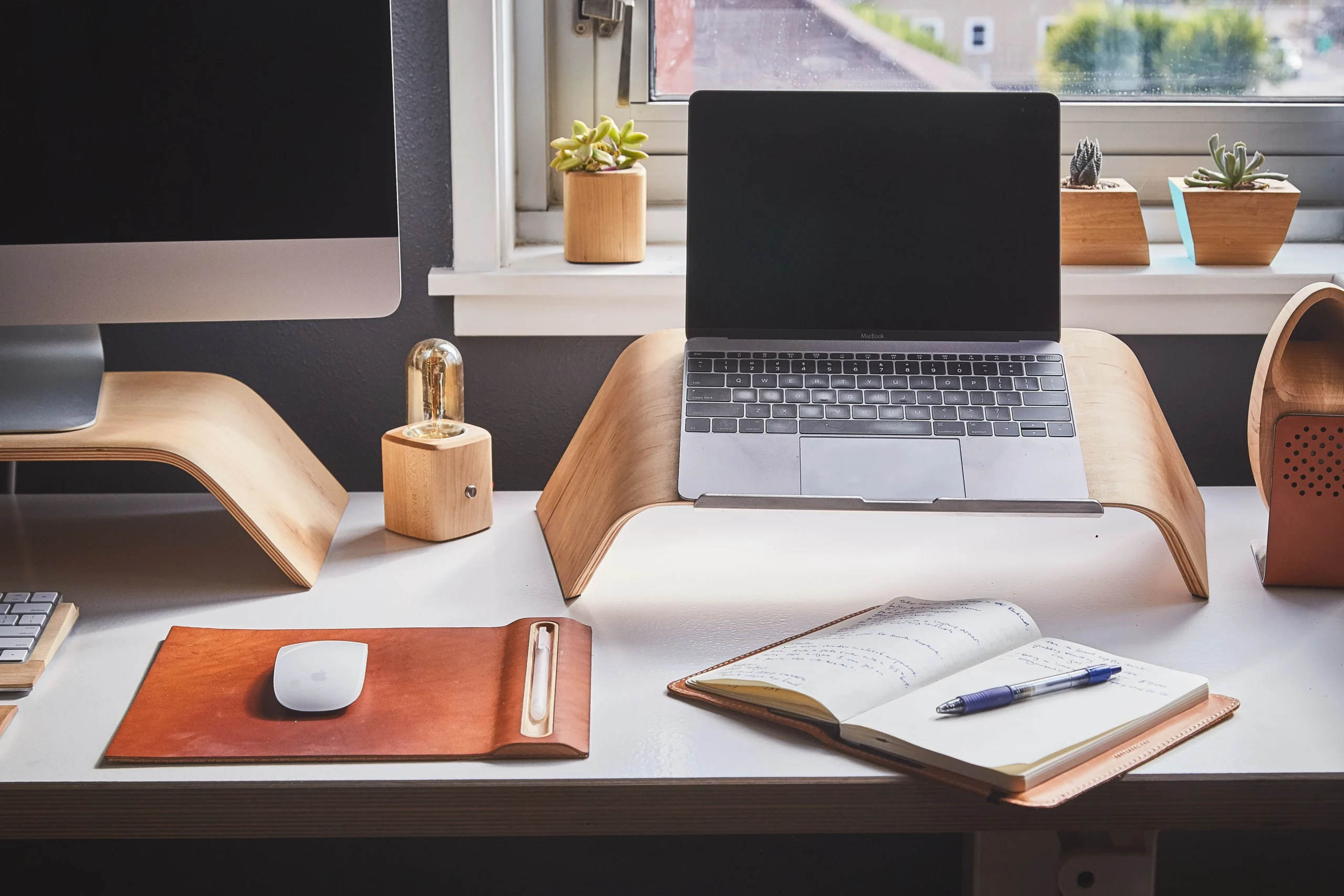 A home-office desk with a laptop whose screen is dark/off, plus a notebook and plants by a window — 6. keep work stuff out of sight at night