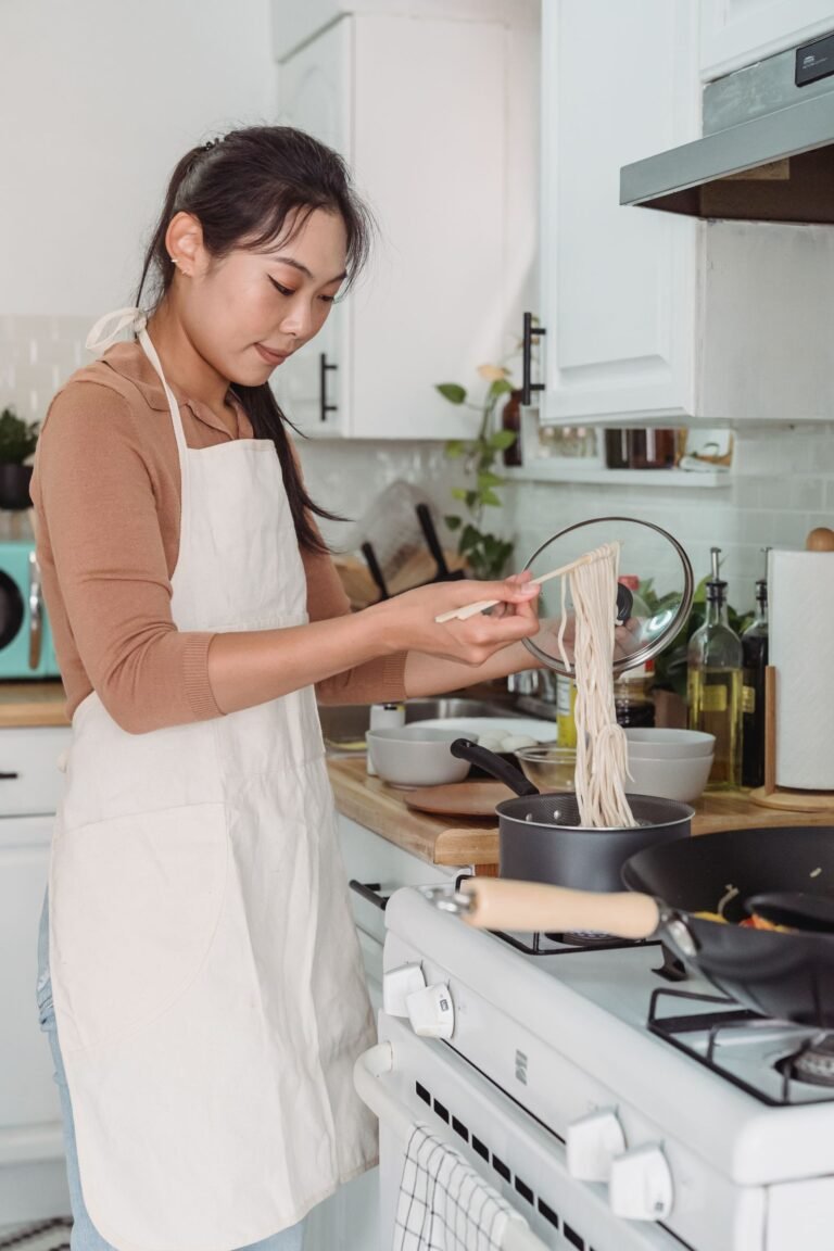 Woman cooking noodles on a stove in a bright small kitchen — small kitchen cooking ideas