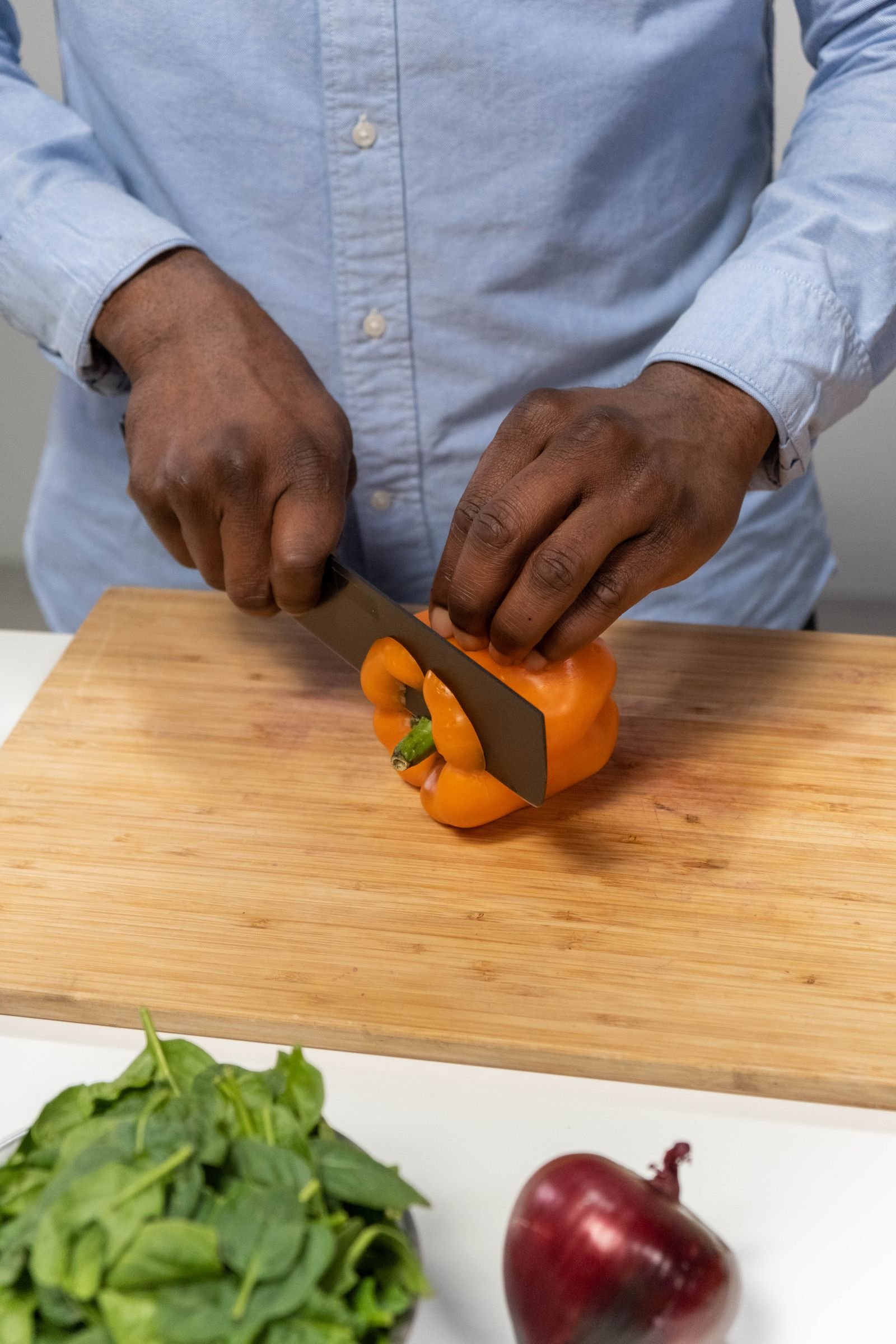 Hands slicing a pepper on a single wooden board — one-board prep for small kitchen cooking