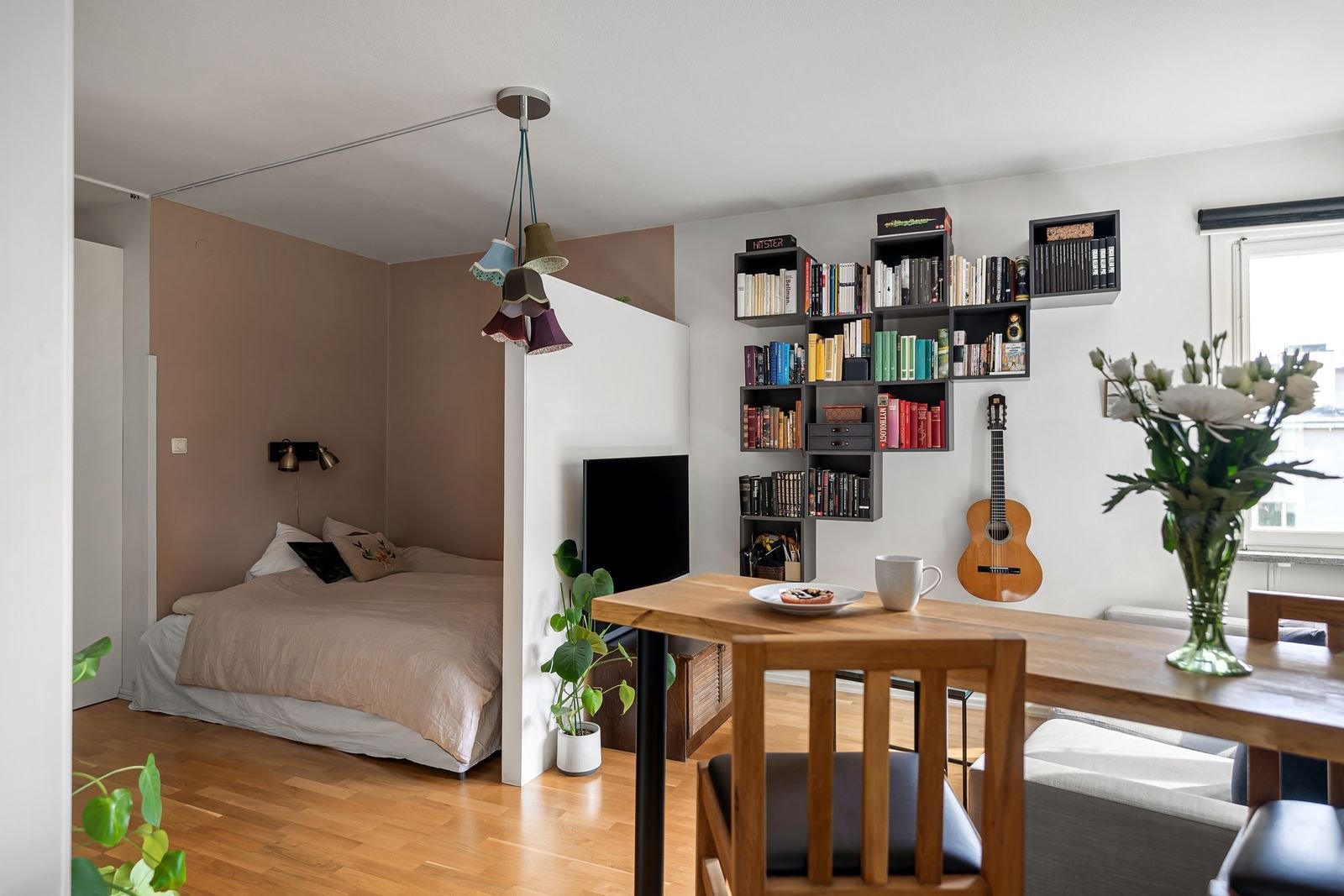 Stylish small studio apartment interior with bed, bookshelf, and decor