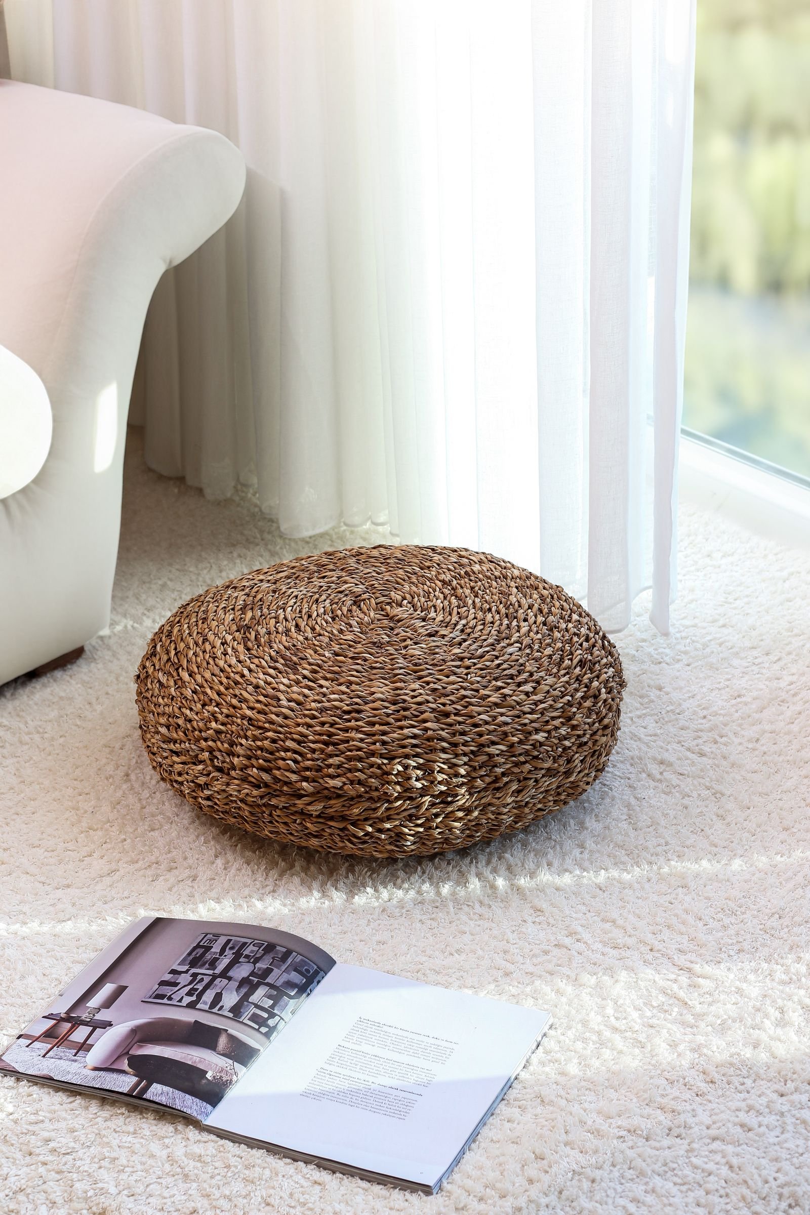 Wicker pouf on shag carpet next to a sofa in a bright living room — stools and poufs tuck away