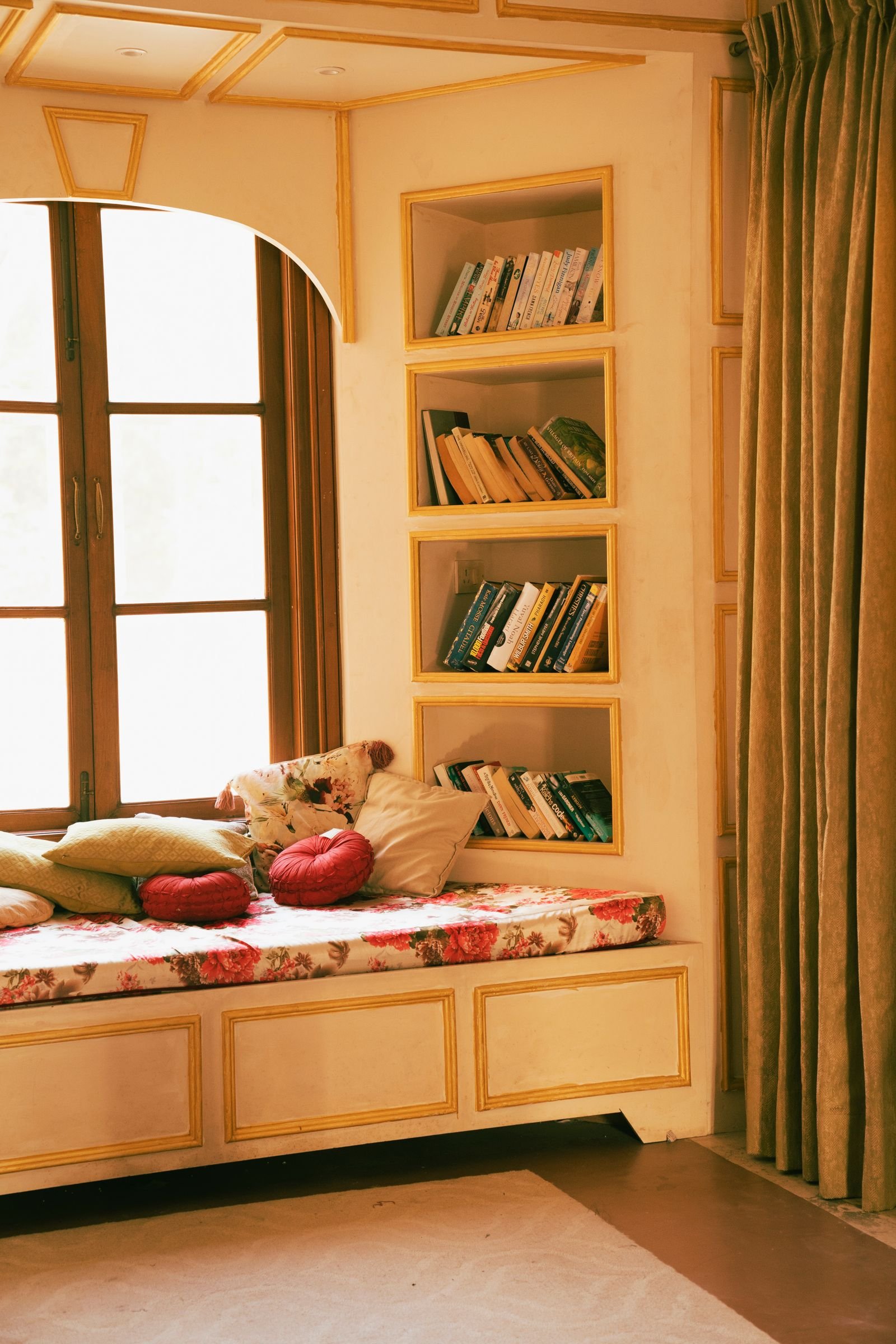 Cozy window seat with floral cushion and pillows beside built-in bookshelves in a bright home interior