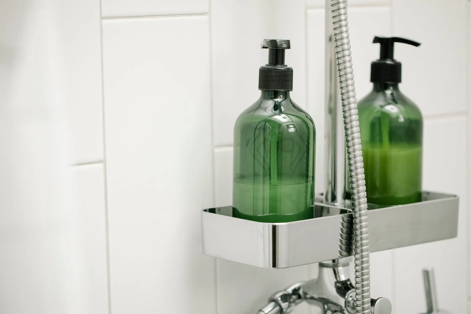 Green dispensers on a shower shelf against a tiled wall — tidy shower bottles for a small bathroom shower