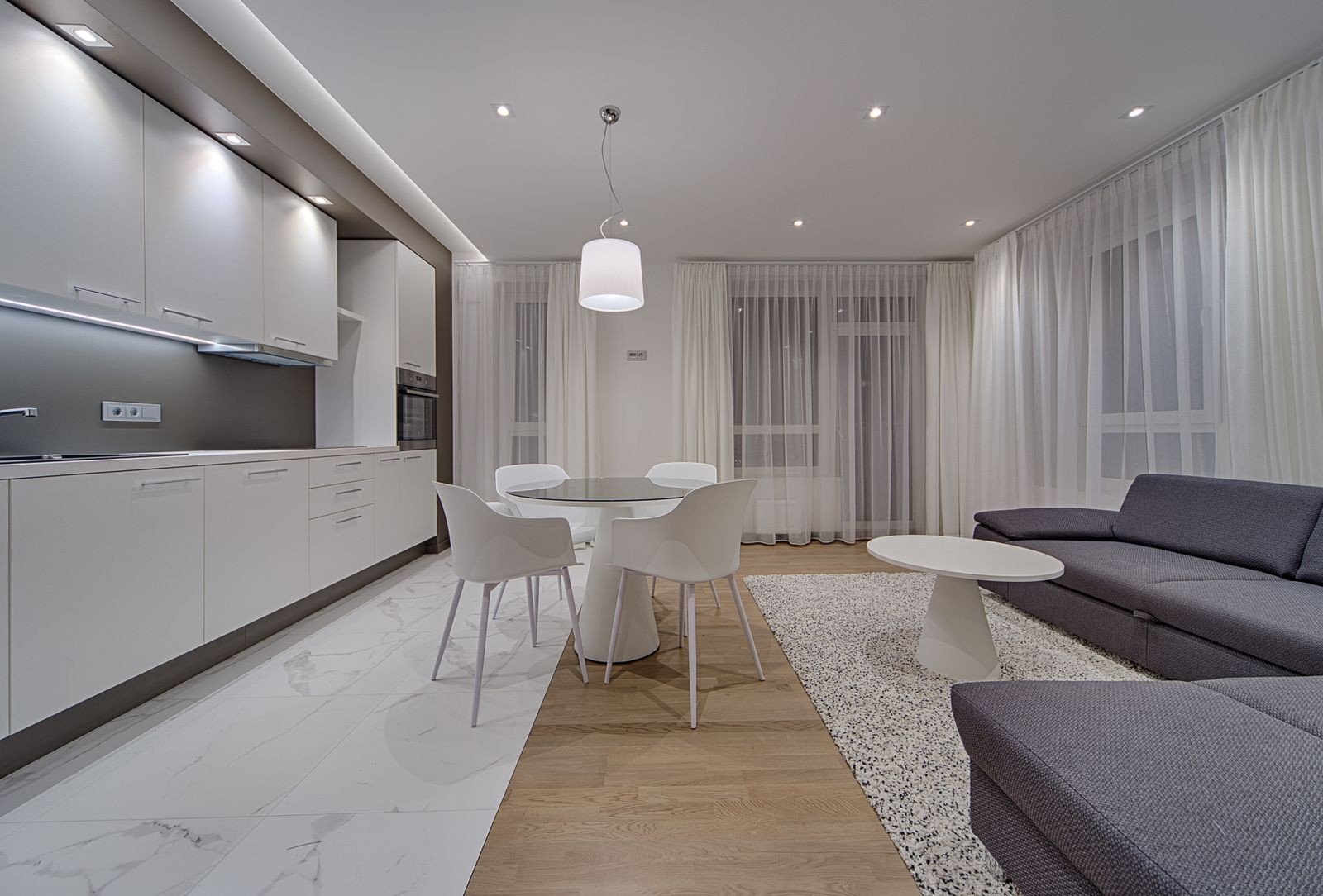Minimalist living room with white closed cabinets and a gray sofa — clutter hidden away behind doors