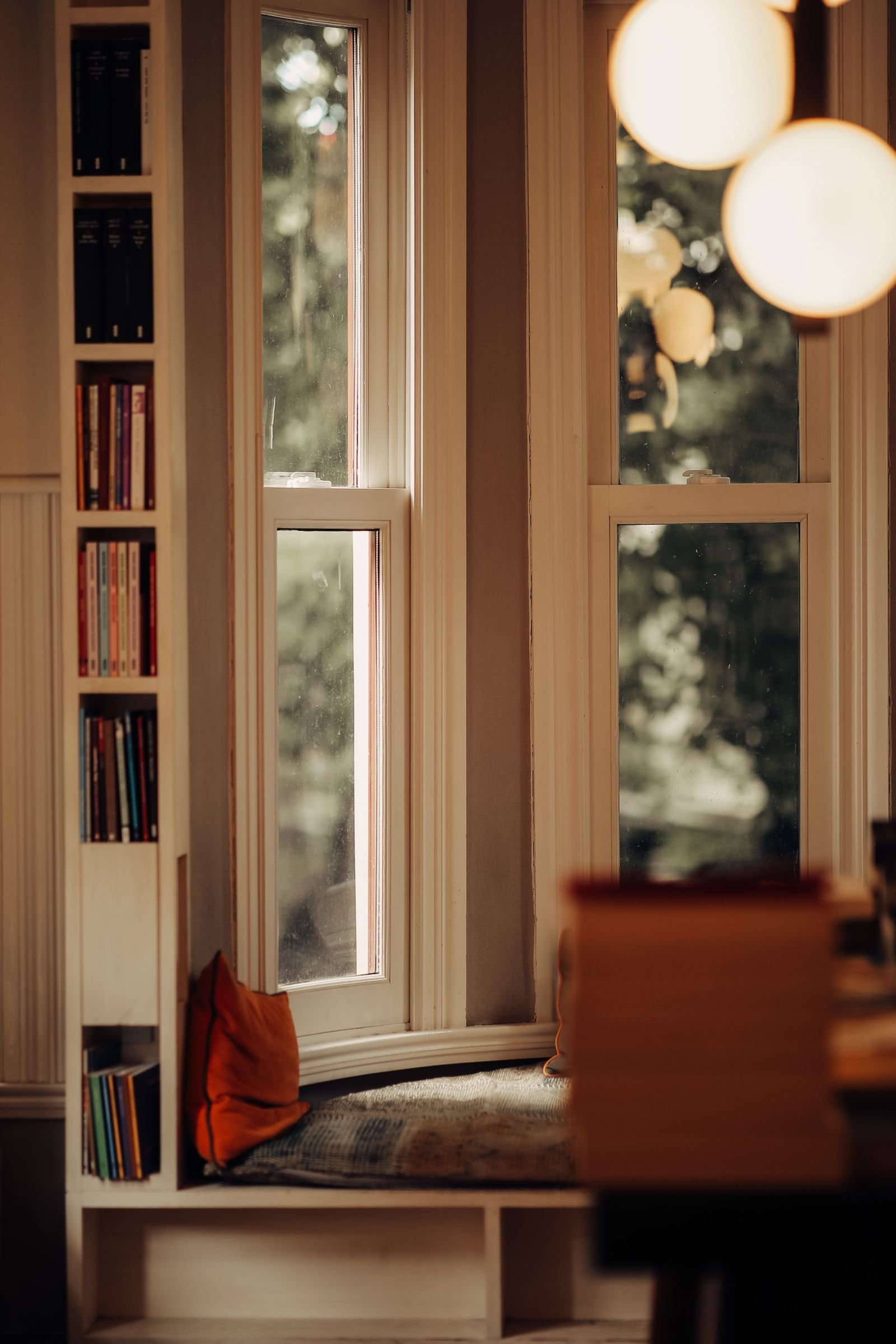 Calm window seat with bookshelf and glowing globe pendant lights in a cozy nook
