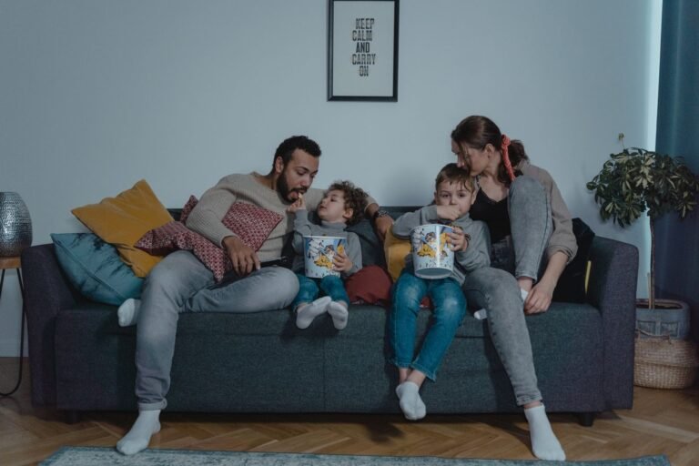 Family sharing popcorn together on a sofa during a cozy movie night in a small living room