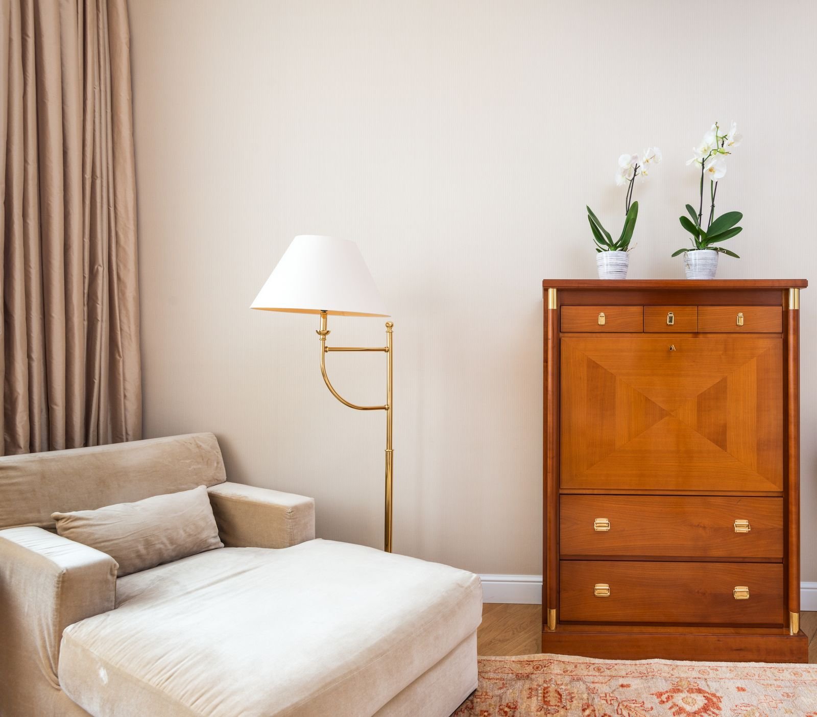 Calm cozy corner with beige armchair, wooden cabinet, soft lighting and potted plants