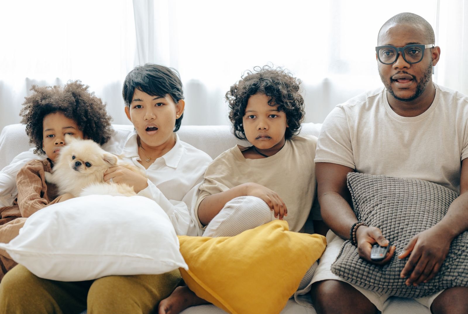Family and their dog sitting together on a couch watching TV straight ahead in a small living room