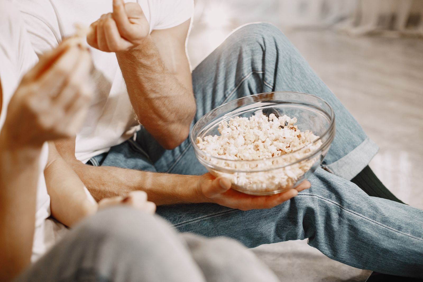Person holding a glass bowl of popcorn, a shared snack setup for a family movie night