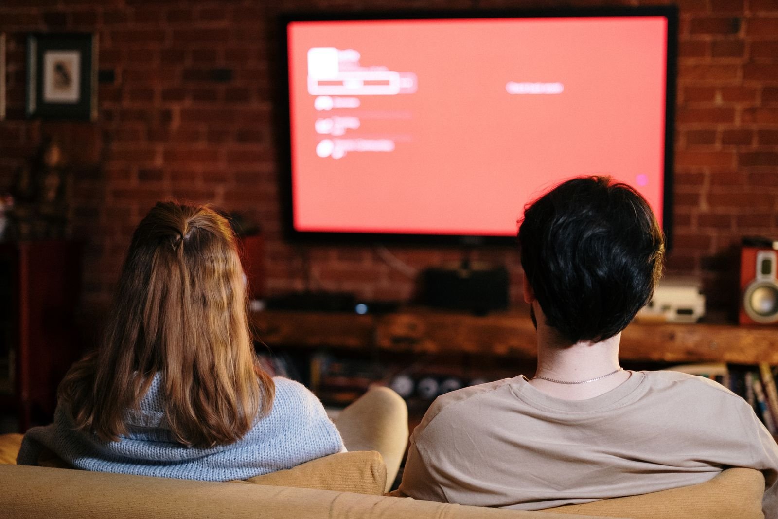 Couple watching TV together on a sofa in a cozy brick-walled living room