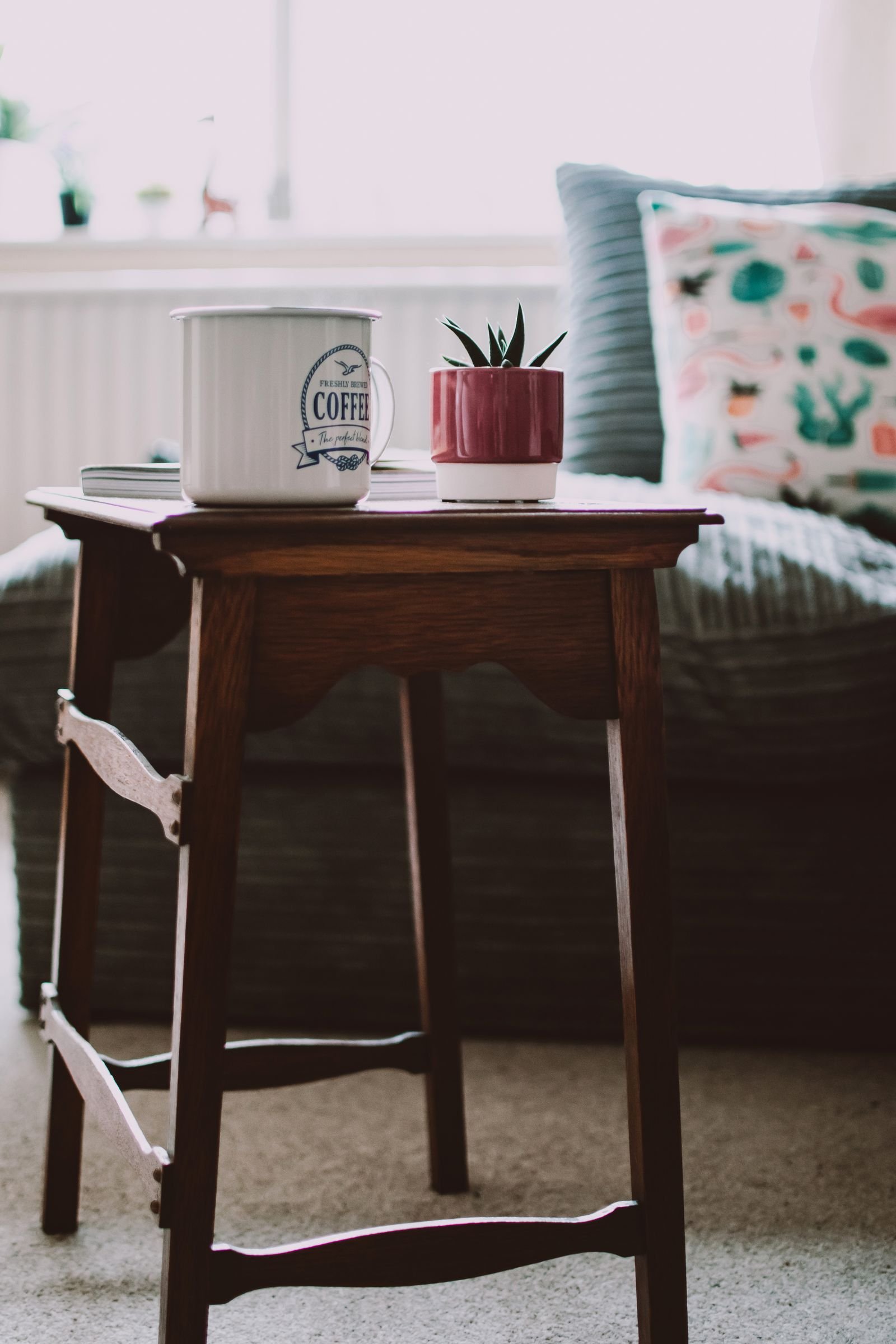White mug on a small wooden side table beside a plant in a living room