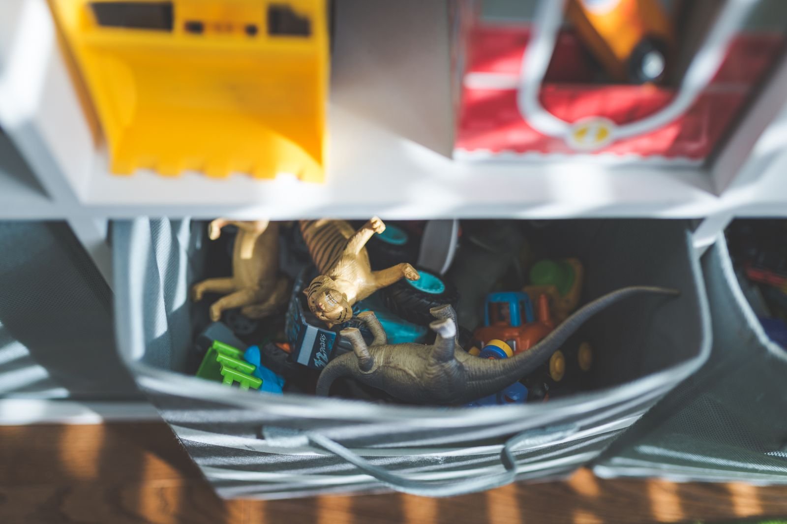 Plastic dinosaurs and toy cars packed inside a storage box in a sunlit room