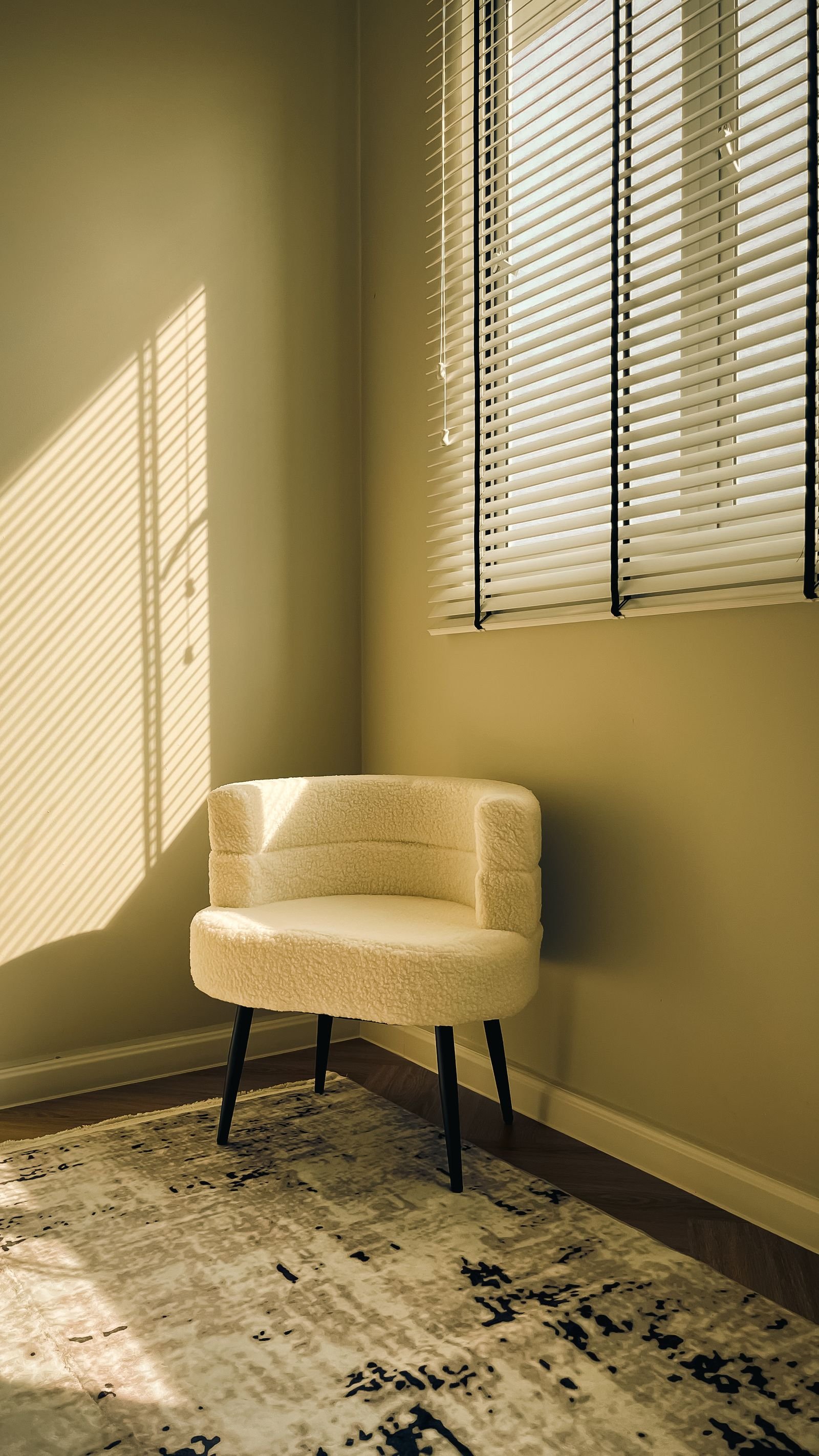 Cream chair in a sunlit corner with blind shadows on the wall
