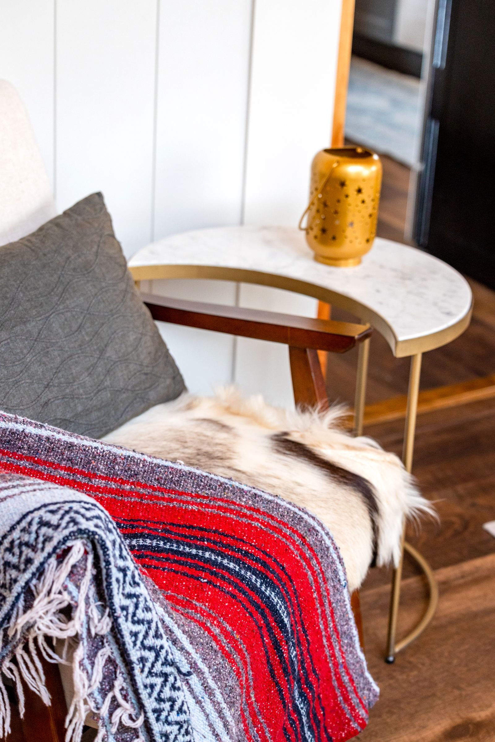 Armchair with vibrant blanket beside a side table and lamp in a cozy corner