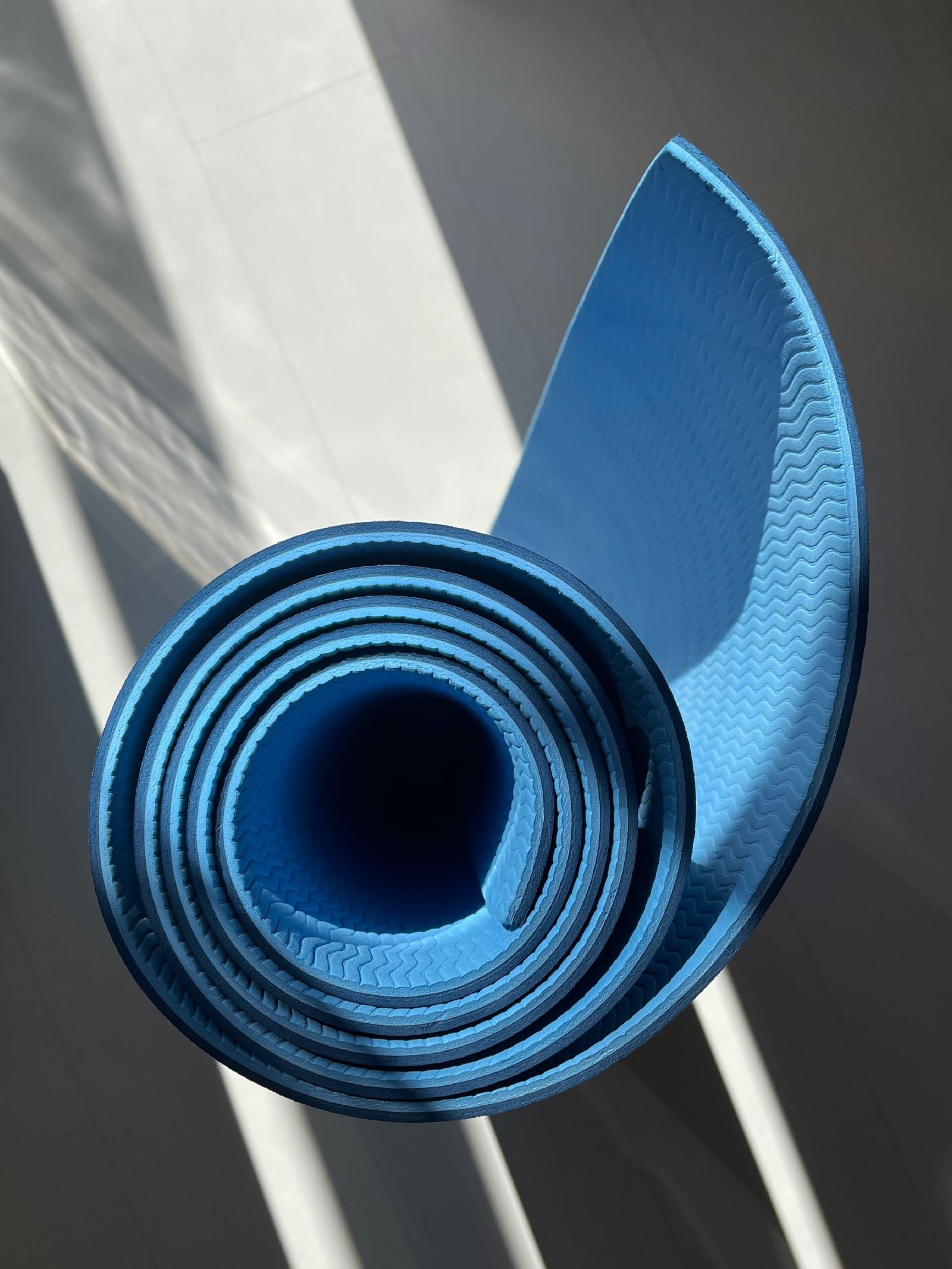 Rolled blue yoga mat resting on a sunlit light floor