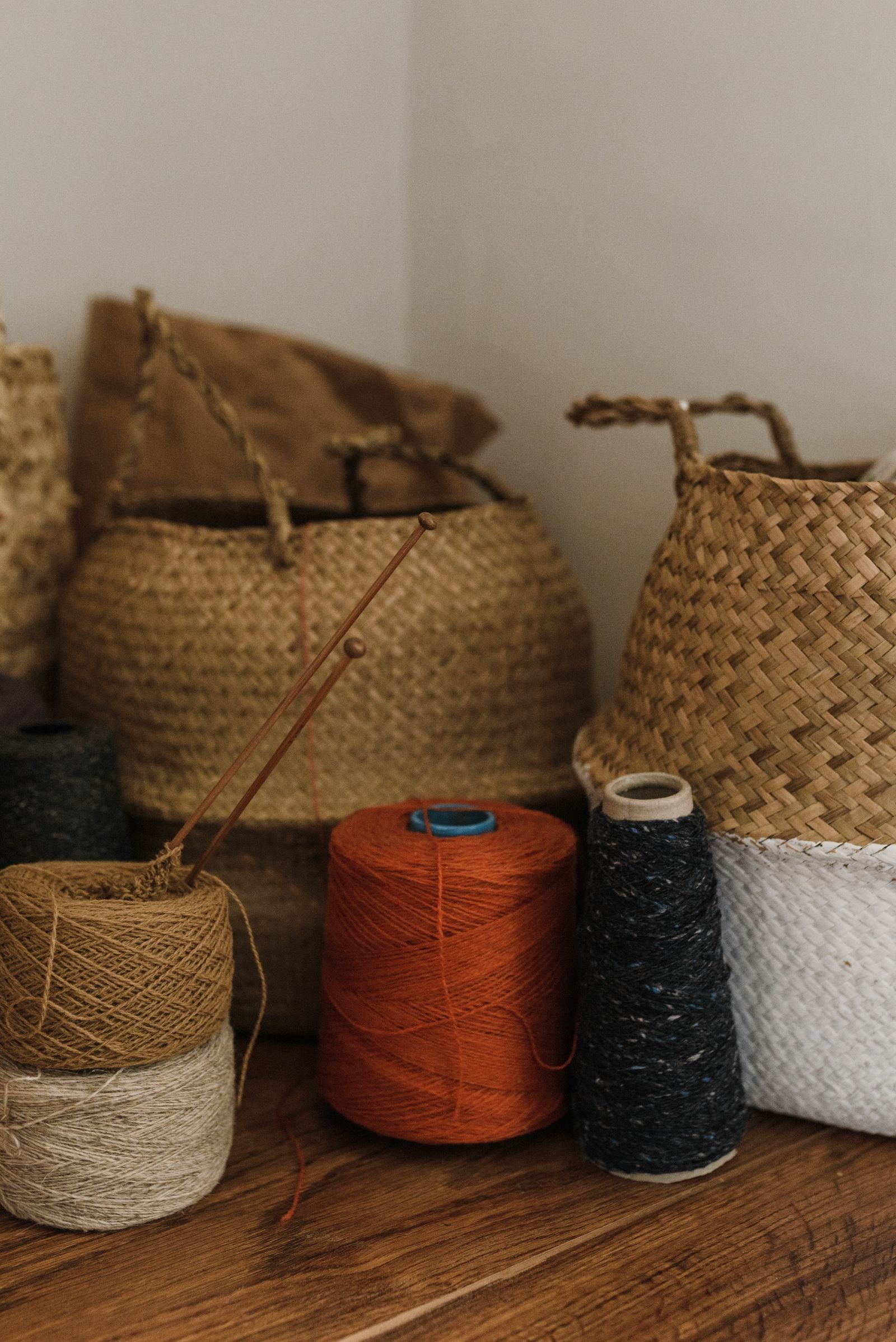 Woven baskets of colorful yarn rolls with knitting needles in a cozy corner