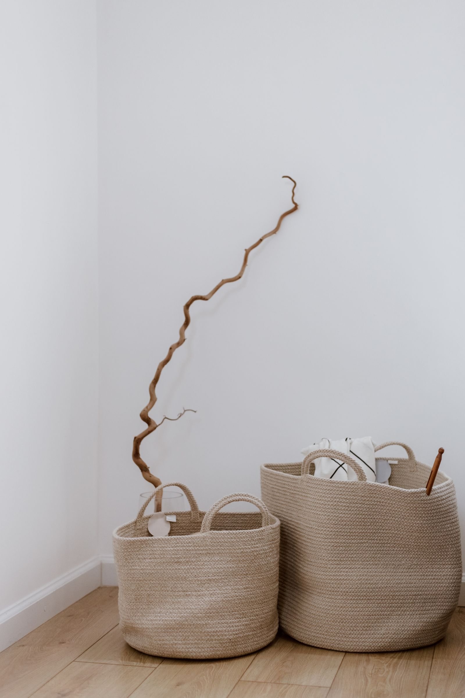 Woven storage baskets lined up in a minimalist white corner on wooden floor