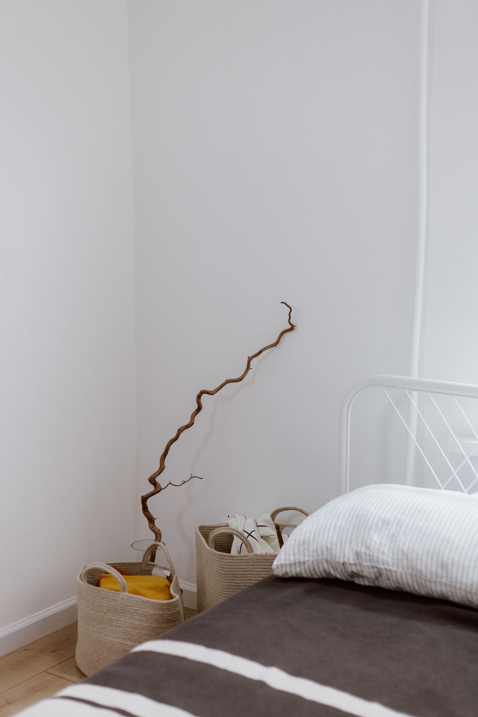 Clean corner with woven baskets and a decorative branch against a white wall